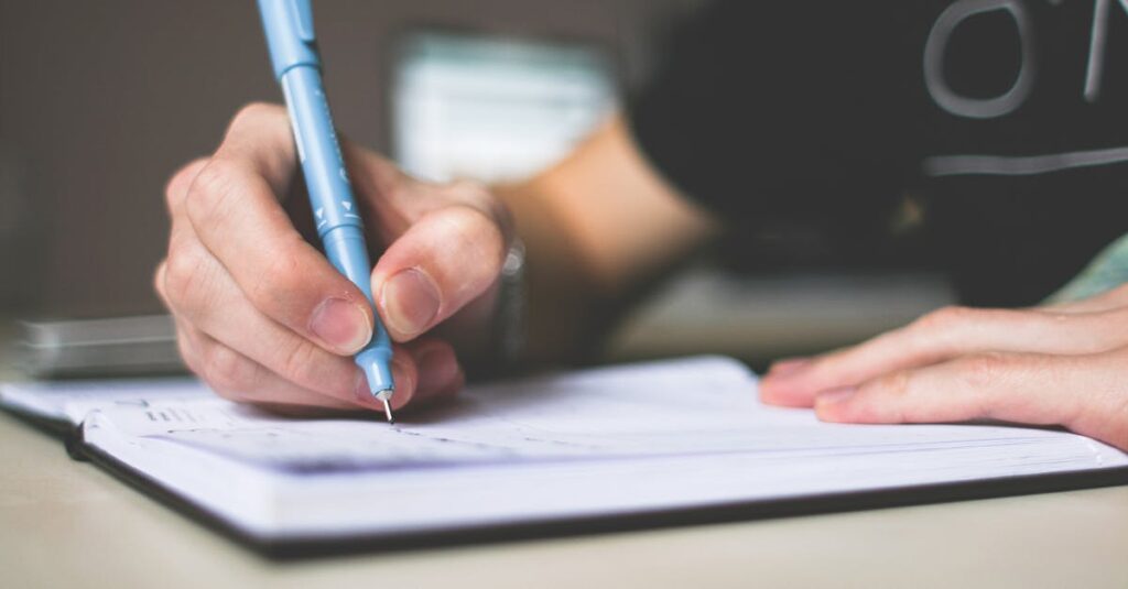 Person Holding Blue Ballpoint Pen Writing in Notebook